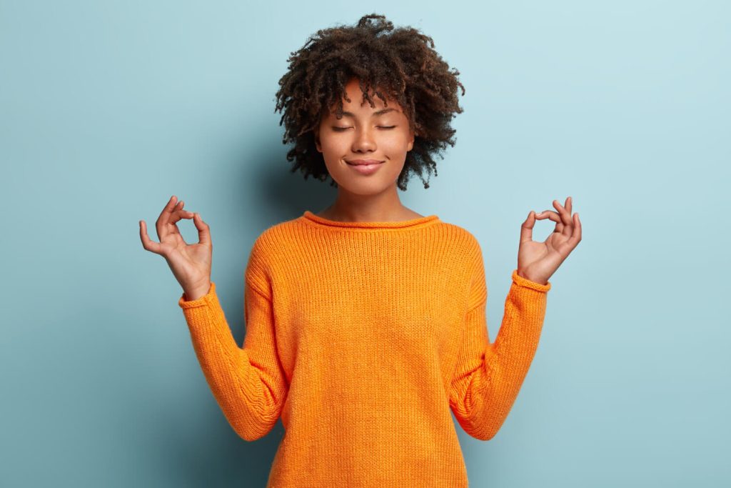 Afro American woman meditates indoor, keeps hands in mudra gesture, has eyes closed as she seeks to use the power of choice